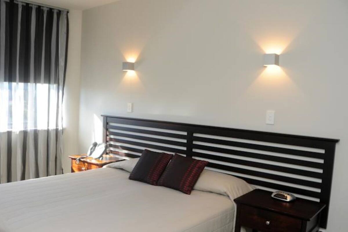 A hotel room with a large bed, two bedside tables, a nightstand, and a window with curtains.
