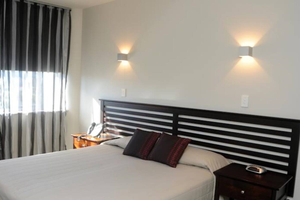 A hotel room with a bed, two bedside tables, a nightstand, and a window with curtains.
