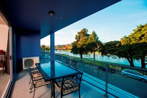 A balcony with a glass table and chairs, overlooking a river and trees. - Emerald Hotel (Gisborne)