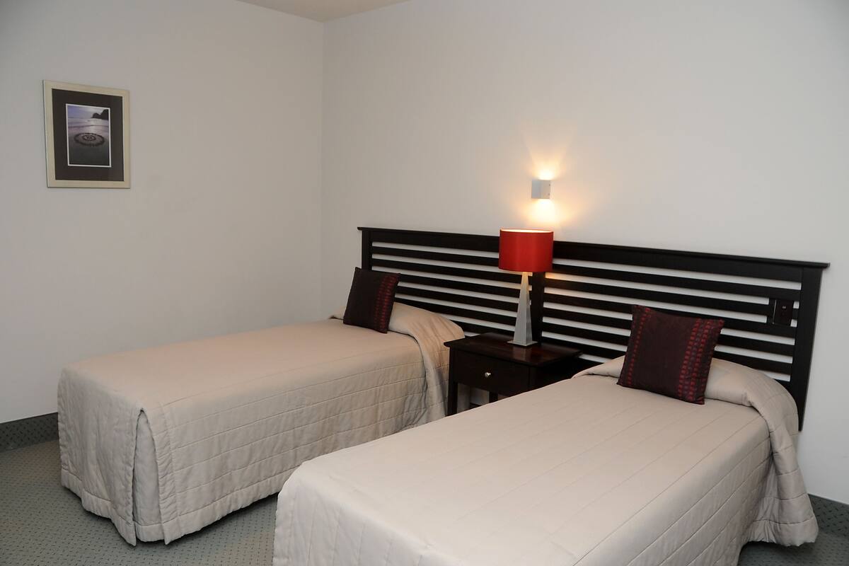 A hotel room with two single beds, a nightstand with a lamp, and a framed picture on the wall.