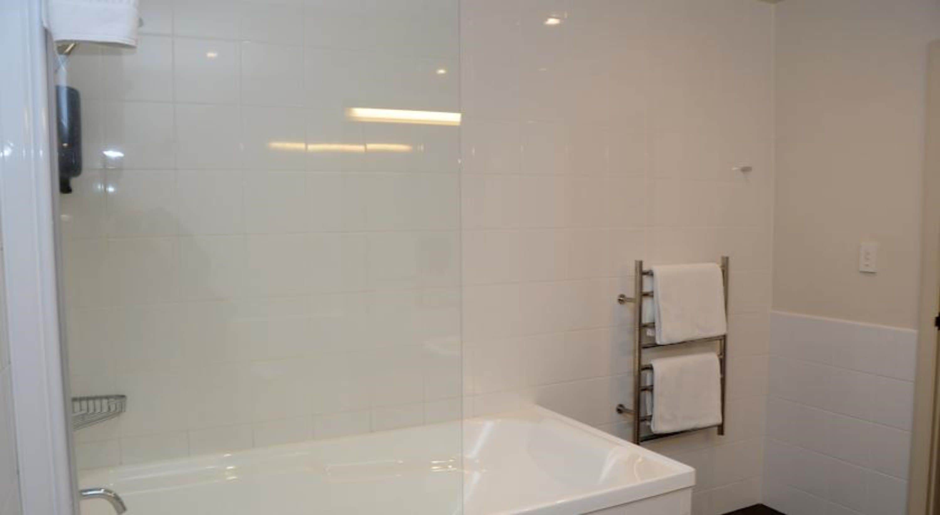 A bathroom with a white bathtub, a glass shower enclosure, and a towel rack with two towels.