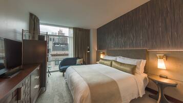 A hotel room with a bed, a TV, a desk, and a view of the city.