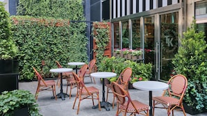 An outdoor seating area with wicker chairs and round tables, surrounded by lush greenery and potted plants. - Marriott Vacation Club®, New York City (New York)