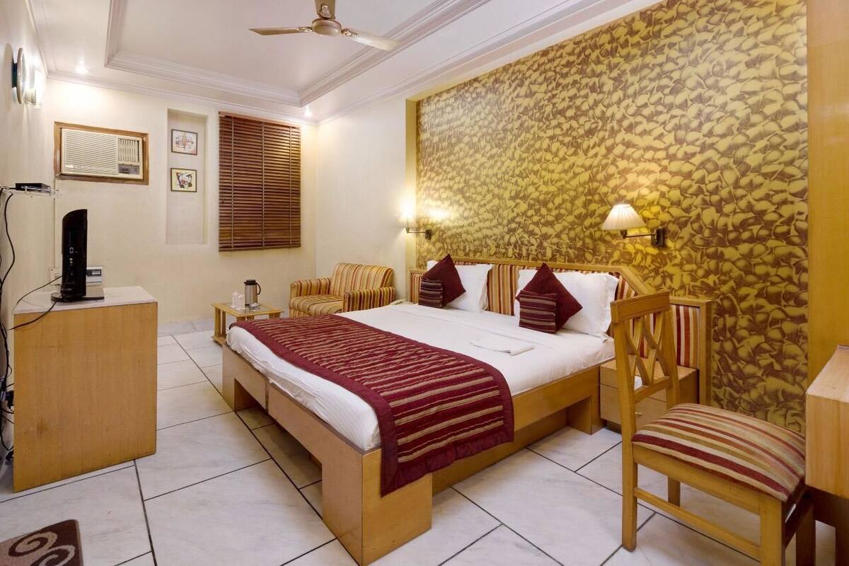 A hotel room with a bed, a desk, a chair, a wall-mounted lamp, and a ceiling fan.