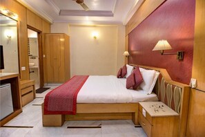 A compact hotel room with a single bed, a small desk, a mirror, and a wardrobe. - Hotel Singh International (New Delhi)