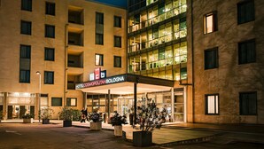 A hotel with a modern facade, multiple balconies, and a well-lit entrance. - Hotel Cosmopolitan Bologna (Bologna)
