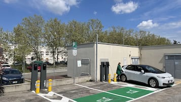 En parkeringsplads med ladestationer til elbil, en cykelsti og et skilt, der angiver døgnåben parkering.