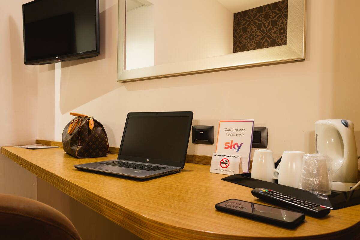 Mostrador de recepción de hotel con una computadora portátil, un control remoto, una cafetera y un letrero que indica que es una habitación para no fumadores.