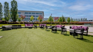 An outdoor seating area with multiple chairs and sofas, a well-maintained lawn, and a building in the background. - Hotel Cosmopolitan Bologna (Bologna)