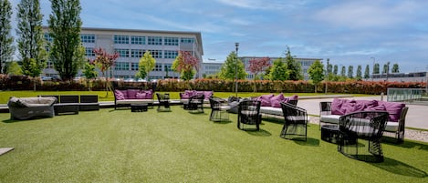 An outdoor seating area with multiple chairs and sofas, a well-maintained lawn, and a building in the background.