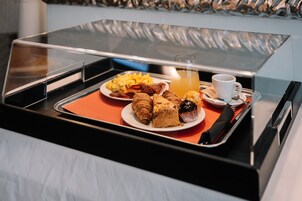 Un vassoio della colazione con croissant, pasticcini, uova strapazzate, pancetta e succo d'arancia, su un vassoio nero con coperchio trasparente.