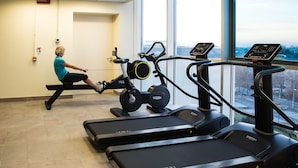 A gym with a rowing machine, treadmills, and a large window with a city view. - Hotel Cosmopolitan Bologna (Bologna)