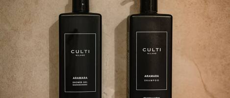 Dos botellas negras de gel de ducha y champú Culti Milano Aramara sobre una pared de baldosas beige.
