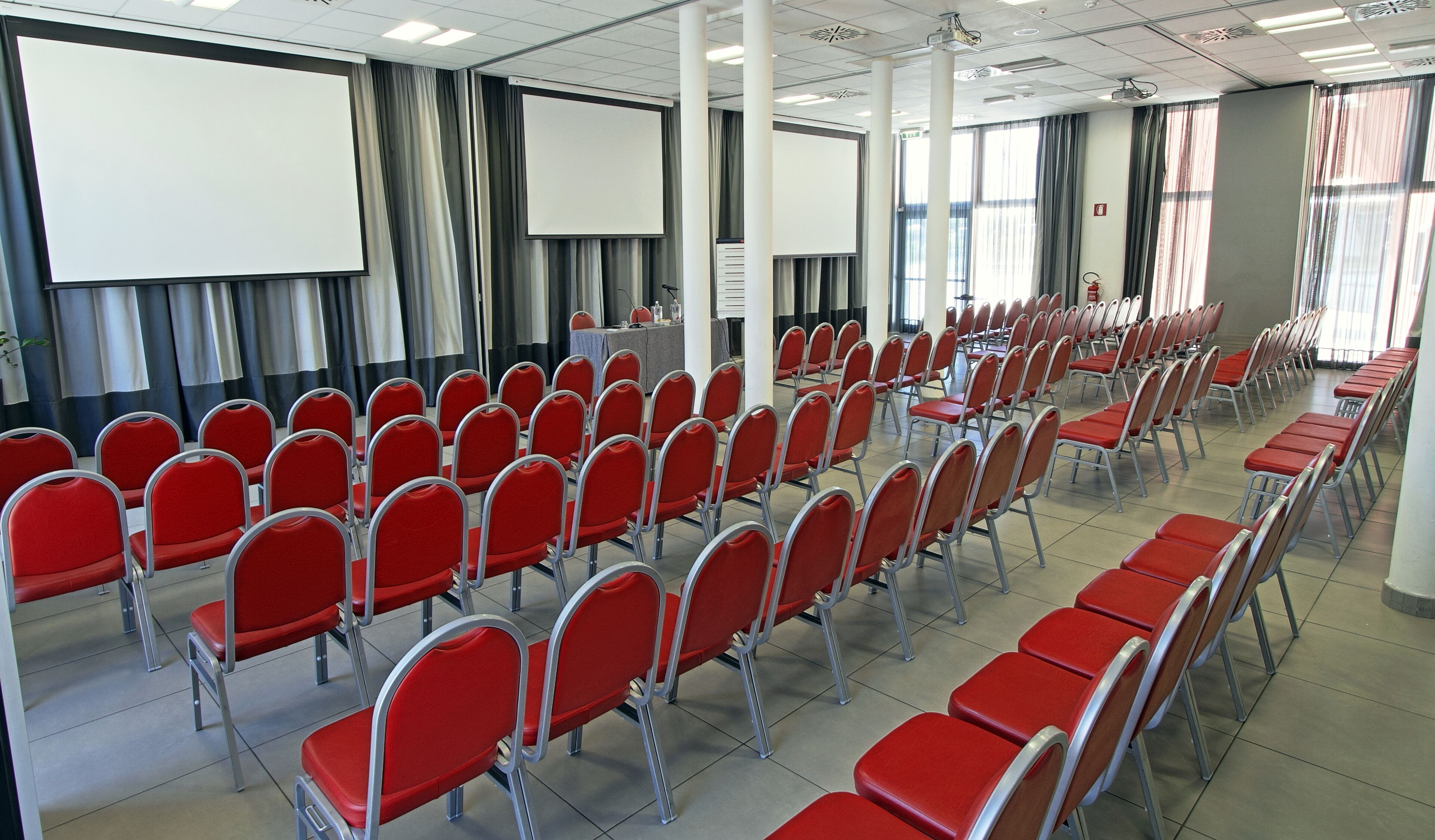 A conference room with rows of red chairs, a projector screen, and a podium.