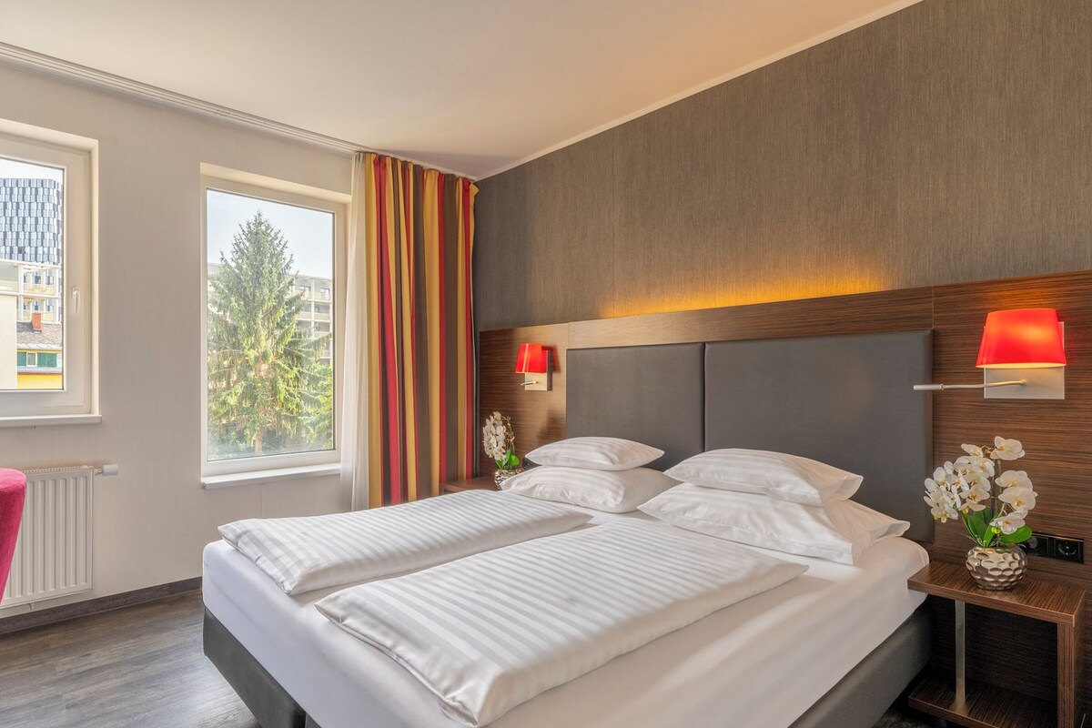 Una habitación de hotel con cama, escritorio, silla, ventana y vistas a edificios.