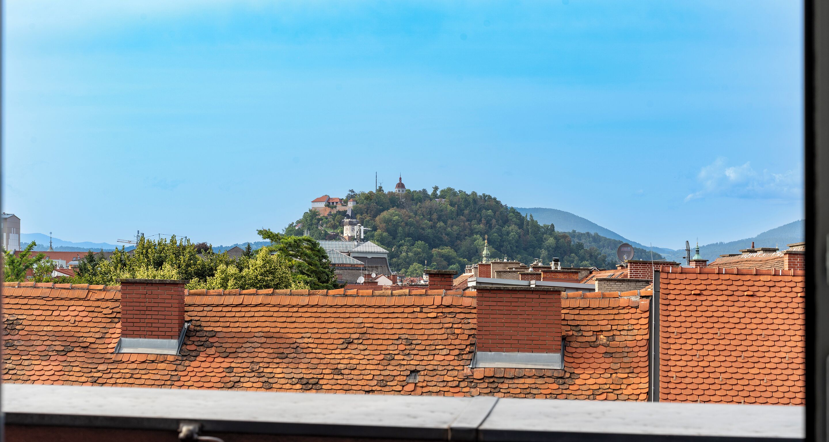 A view of a hilltop building with a dome, surrounded by greenery and other buildings.