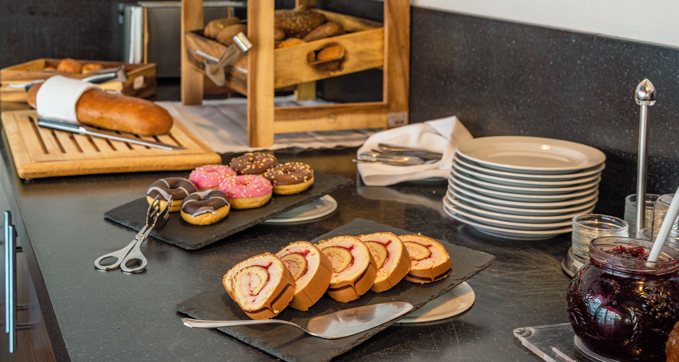 A breakfast buffet with pastries, a loaf of bread, and a jar of jam.