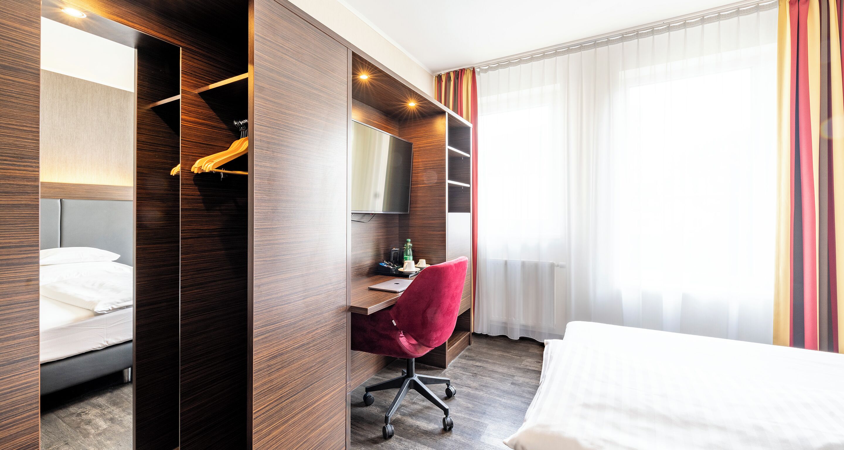 A hotel room with a bed, a desk, a chair, a TV, and a wardrobe.