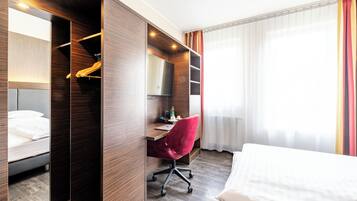 A hotel room with a bed, a desk, a chair, a TV, and a wardrobe.
