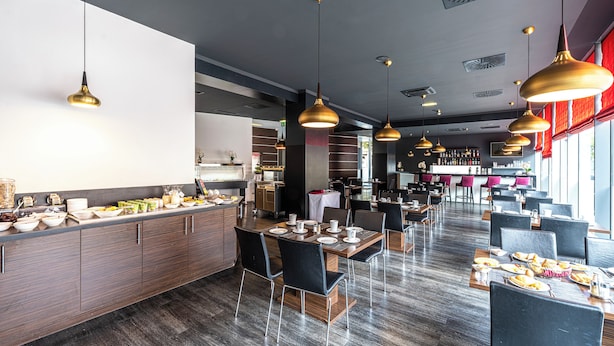 Un comedor moderno con varias mesas, sillas negras e iluminación colgante dorada.