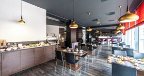 Un comedor moderno con varias mesas, sillas negras e iluminación colgante dorada.