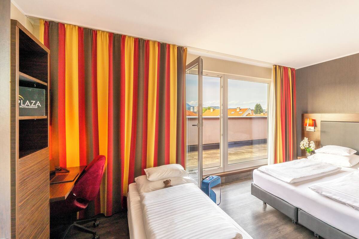 Une chambre d’hôtel avec un lit, un bureau, une chaise, une télévision et une vue sur la ville par la fenêtre.