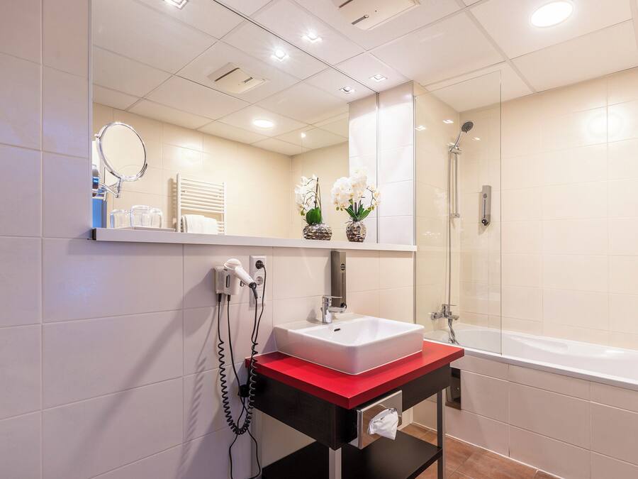 Un baño moderno con un lavabo blanco, una encimera roja, una ducha con mampara de cristal y un espejo sobre el lavabo.