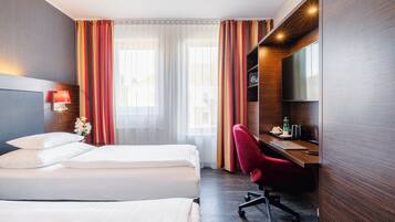 A hotel room with two beds, a desk with a chair, a TV, and a window with curtains.