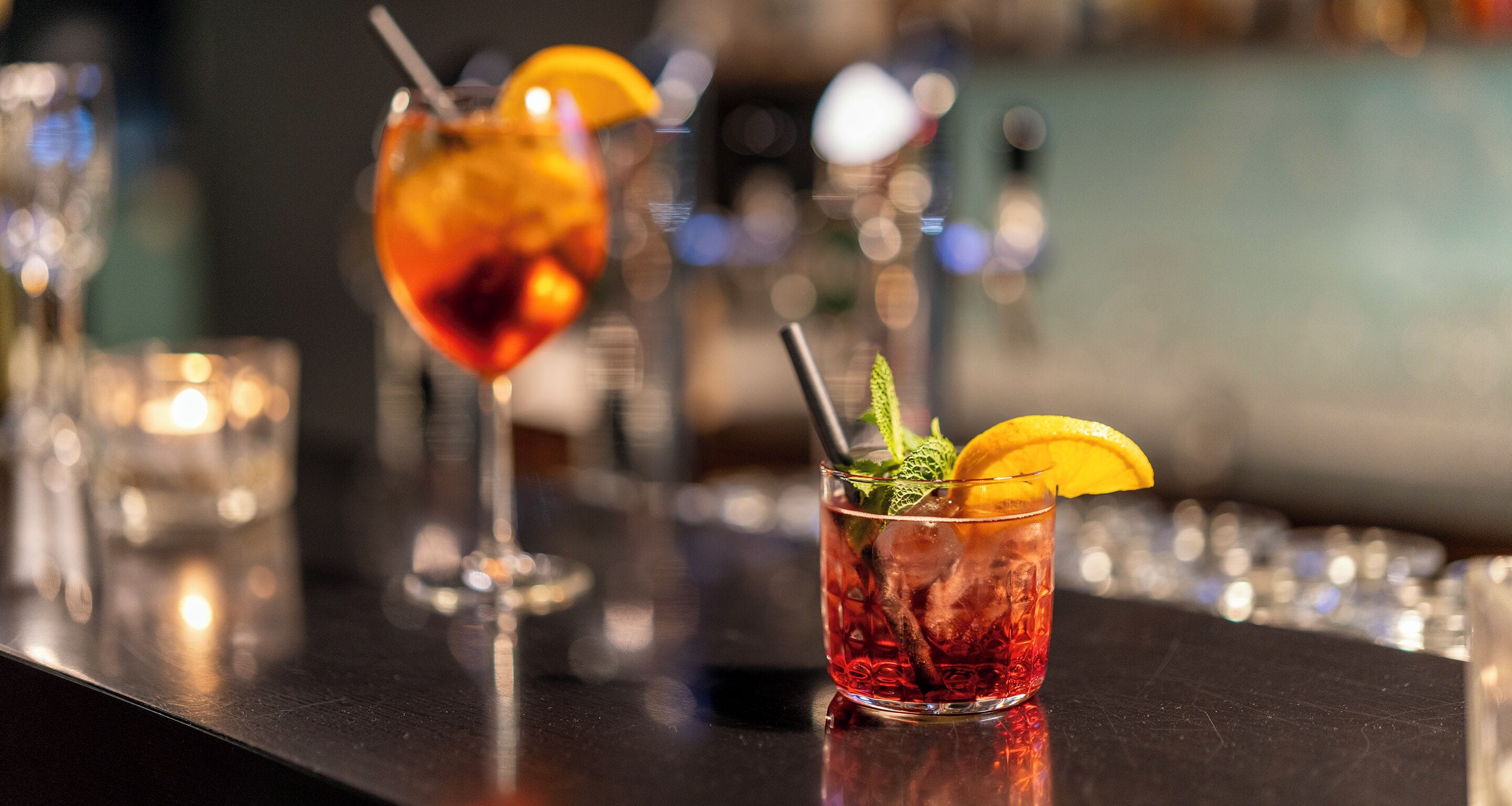 Two cocktails on a bar counter with a blurred background.