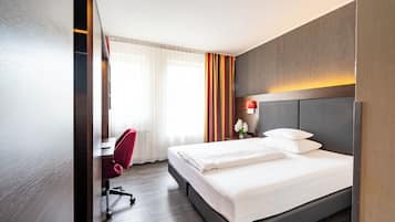 Una habitación de hotel con cama, escritorio, silla y ventana con cortinas.