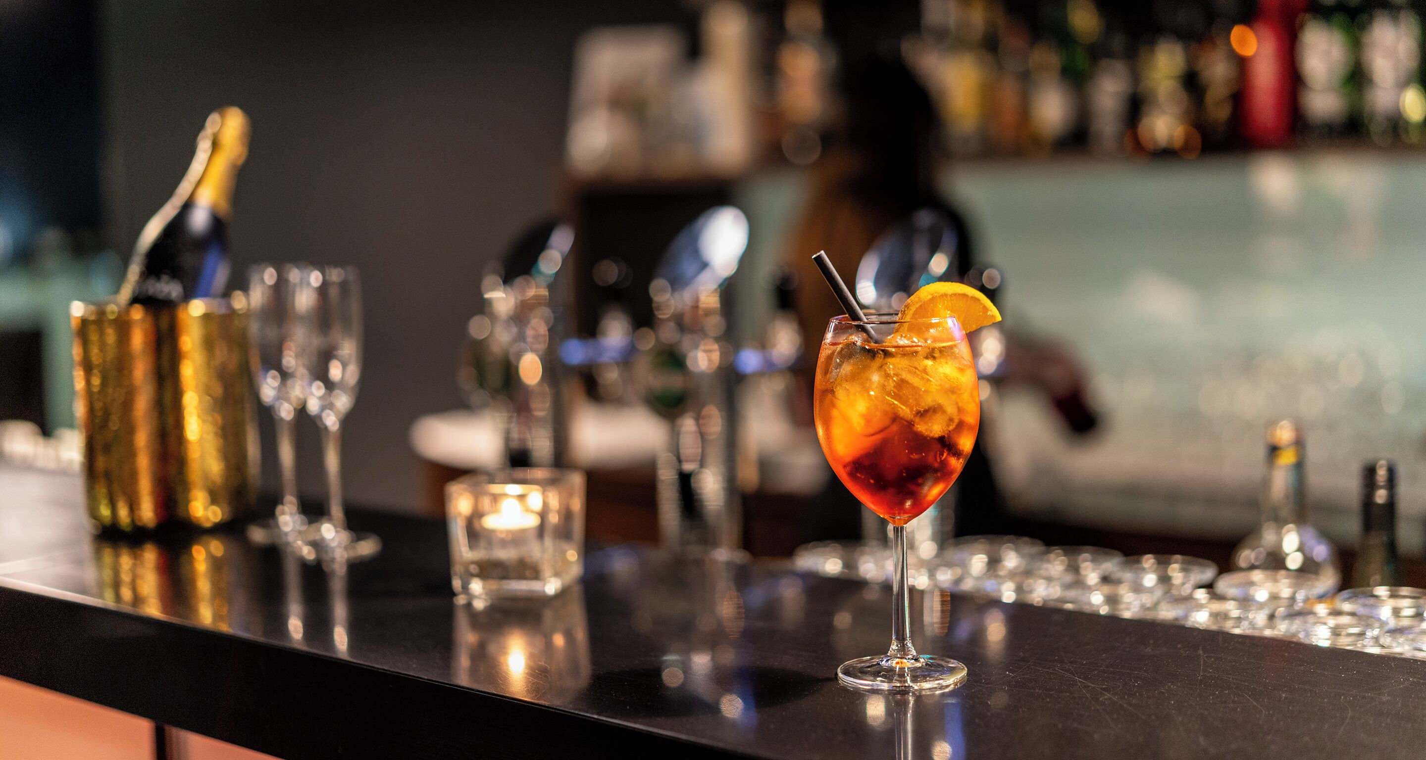 Eine Bar mit einem Cocktailglas, einer Champagnerflasche und einer Kerze.