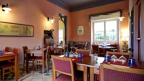 A dining area with wooden tables and chairs, a large framed picture on the wall, and a window with curtains. - Hotel Del Borgo (Sestri Levante)