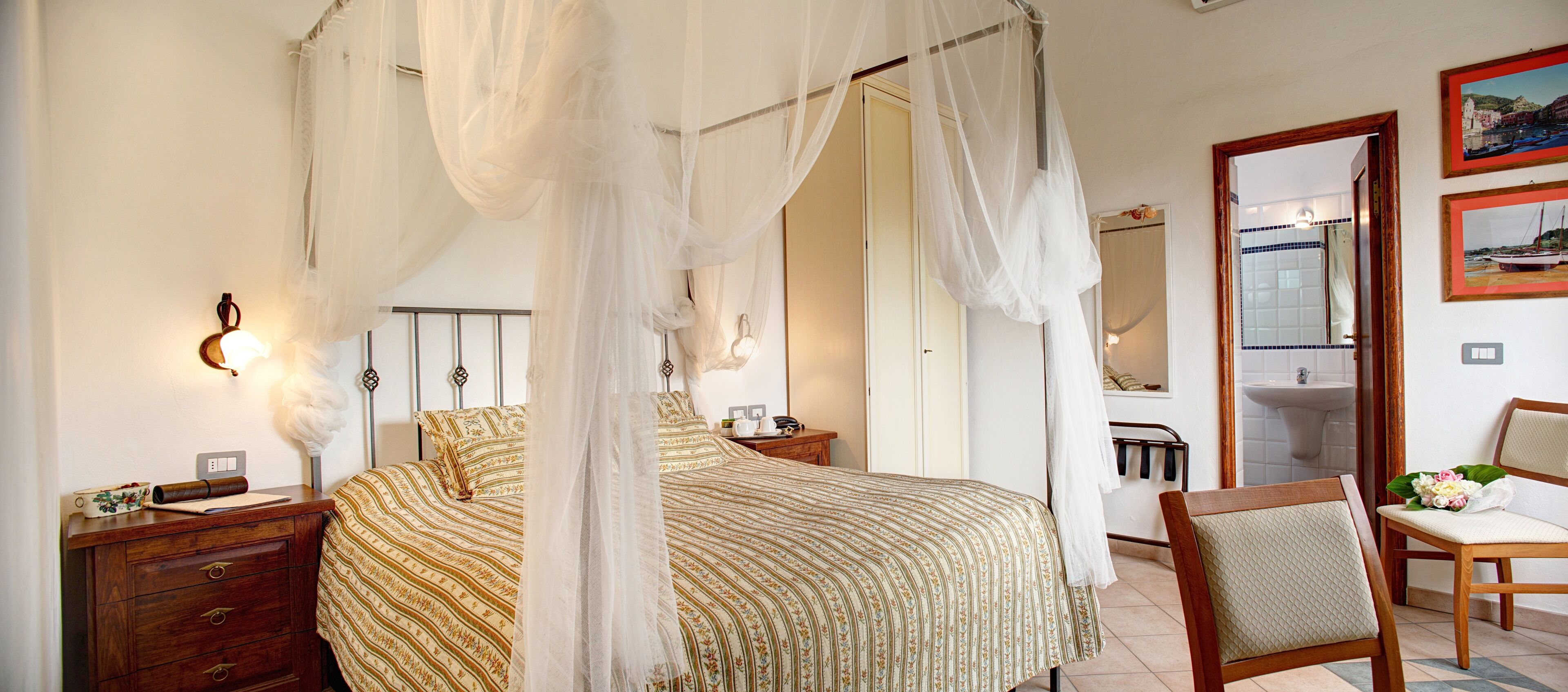 A bedroom with a four-poster bed, a wooden nightstand, a chair, a bedside table, and a mirror.