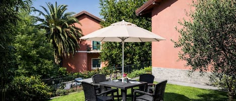 Un patio exterior con una mesa y sillas, rodeado de exuberante follaje y un edificio al fondo.