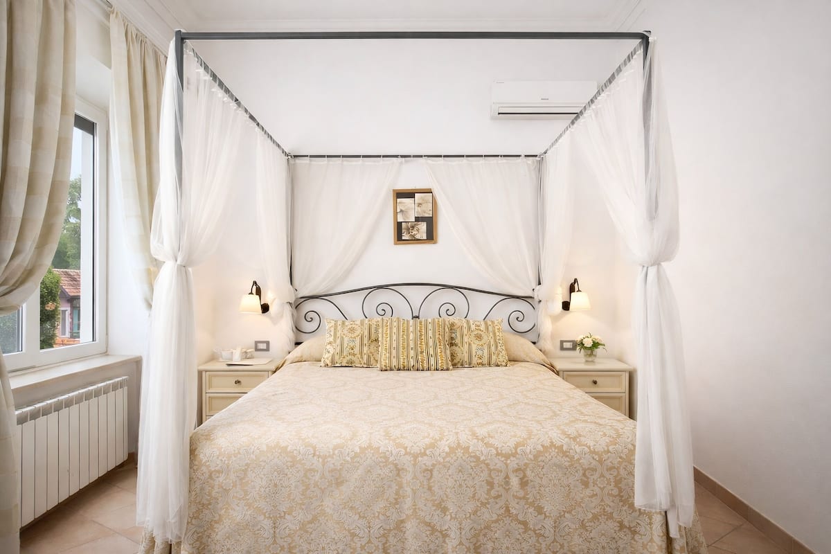 Una cama con dosel y cuatro columnas, cubierta con una colcha estampada, lámparas de noche y un cuadro en la cabecera.