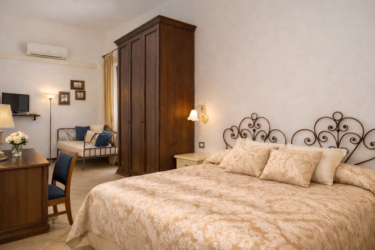 Un dormitorio con una cama grande, un escritorio con lámpara, una silla, un armario y un televisor sobre un mueble.