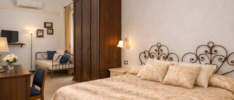 Un dormitorio con una cama grande, un escritorio con lámpara, una silla, un armario y un televisor sobre un mueble.