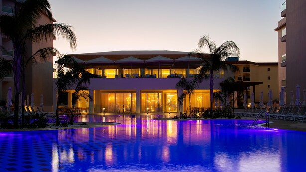 A hotel with a swimming pool, lounge chairs, and palm trees. - Vangelis Hotel & Suites (Paralimni)
