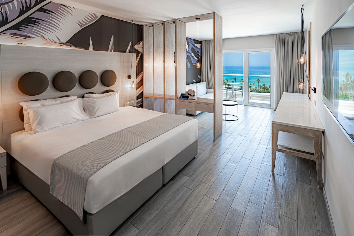 Une chambre d’hôtel moderne dotée d’un grand lit, d’un bureau et d’un balcon offrant une vue sur l’océan.