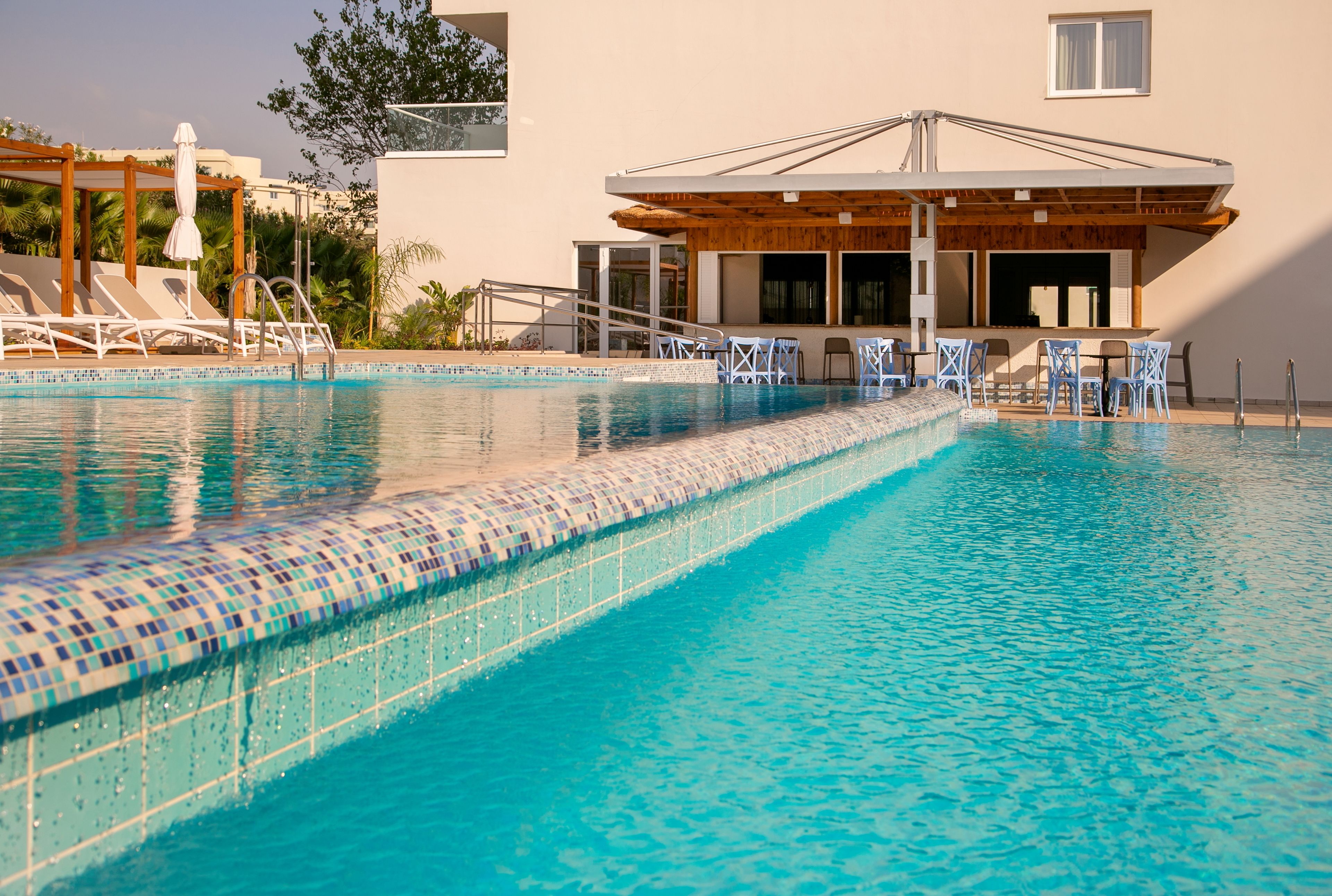 A swimming pool with tiled edges, lounge chairs, and a covered seating area with tables and chairs.