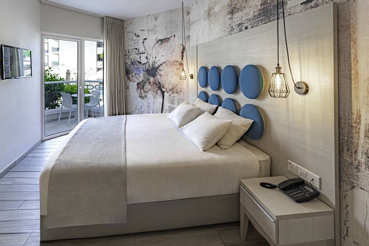 Une chambre d’hôtel moderne avec un grand lit, un téléphone sur la table de chevet et une vue sur le balcon.