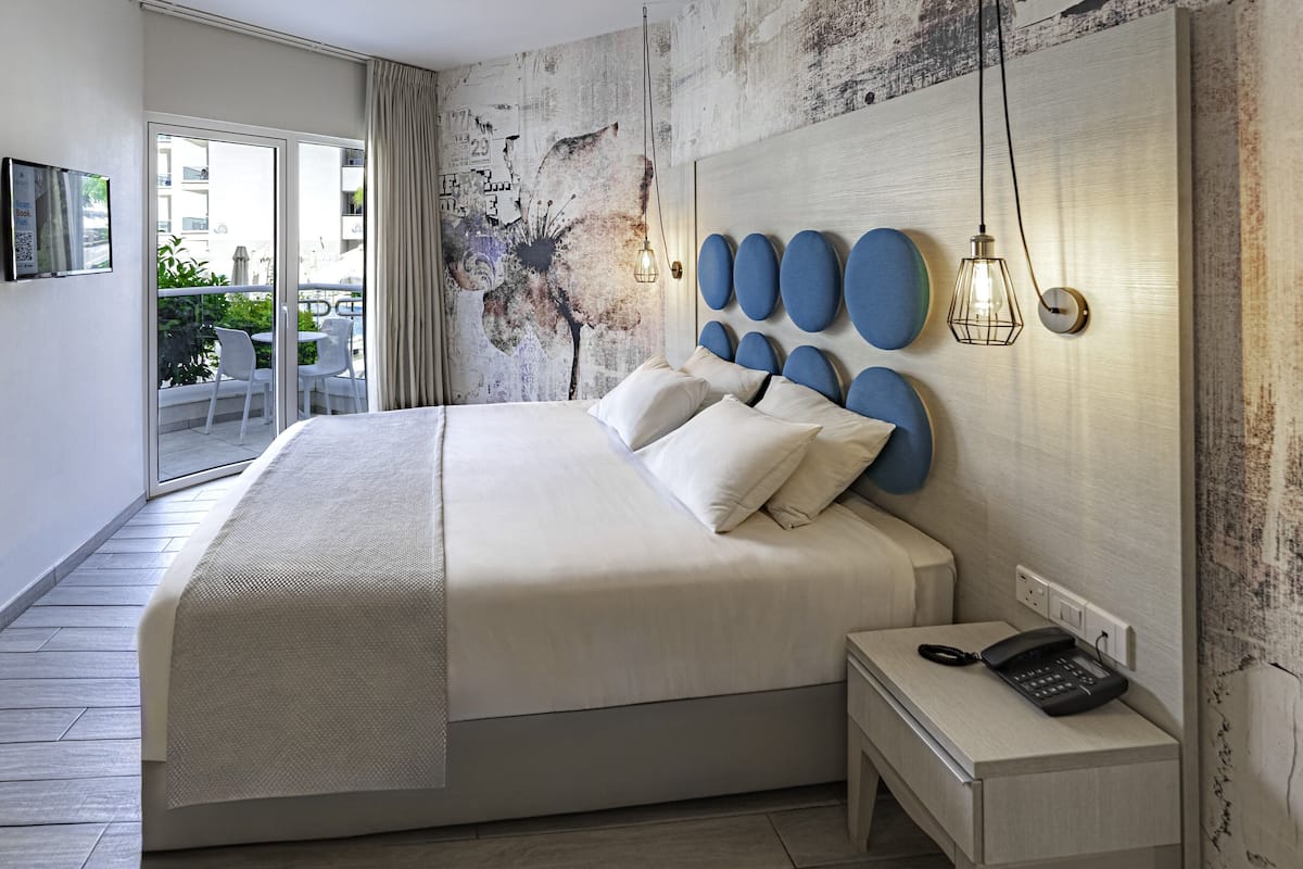 Una habitación de hotel moderna con una cama grande, un teléfono en la mesita de noche y vistas al balcón.