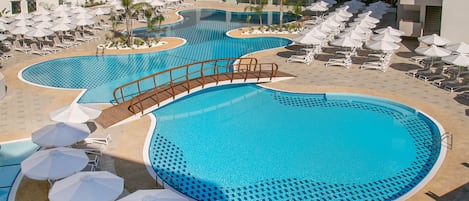 A resort pool area with multiple swimming pools, sun loungers, and umbrellas.