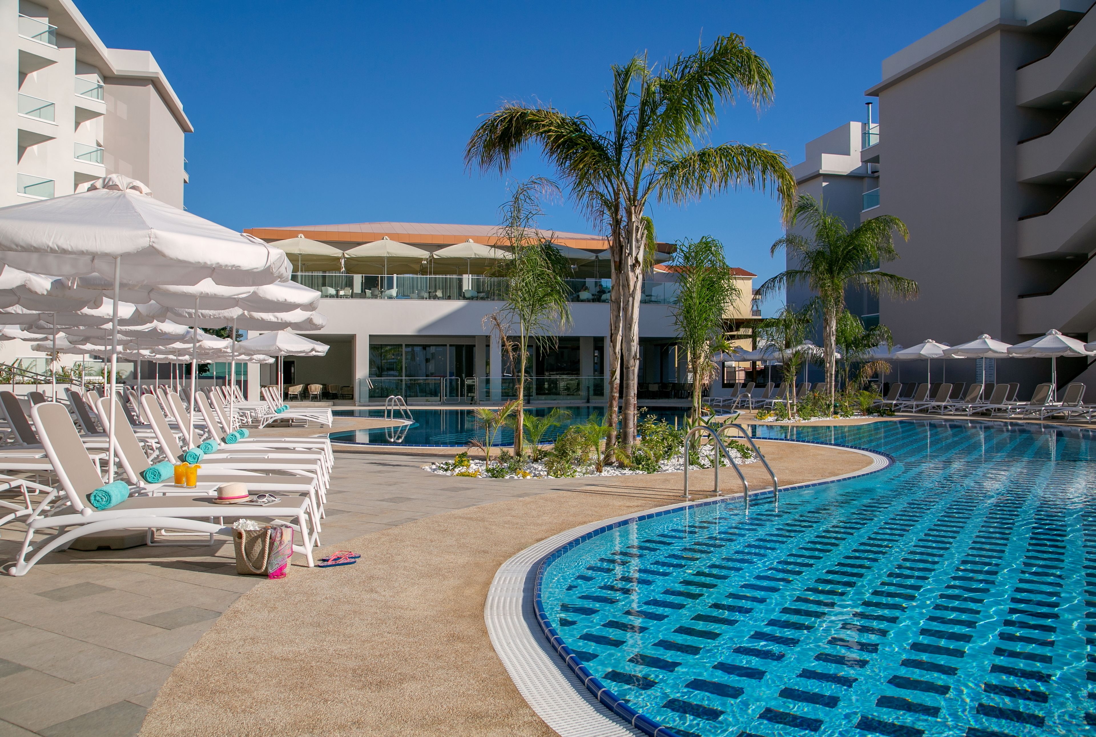 A poolside area with lounge chairs, umbrellas, and palm trees.