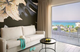 A modern living room with a sofa, a round table with apples, and a view of the sea.