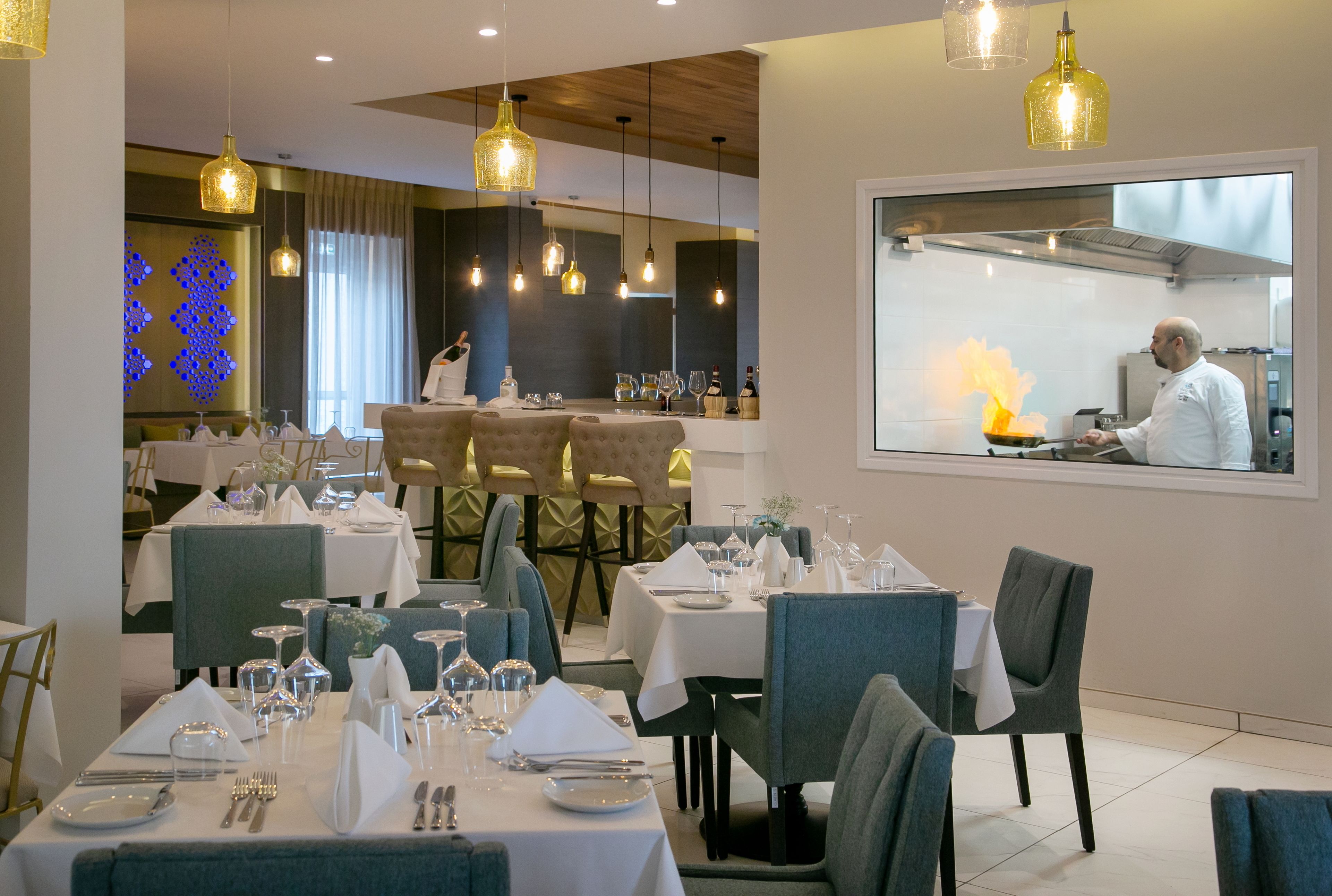 Een eetruimte met gedekte tafels, een kok in de keuken en een modern interieur.