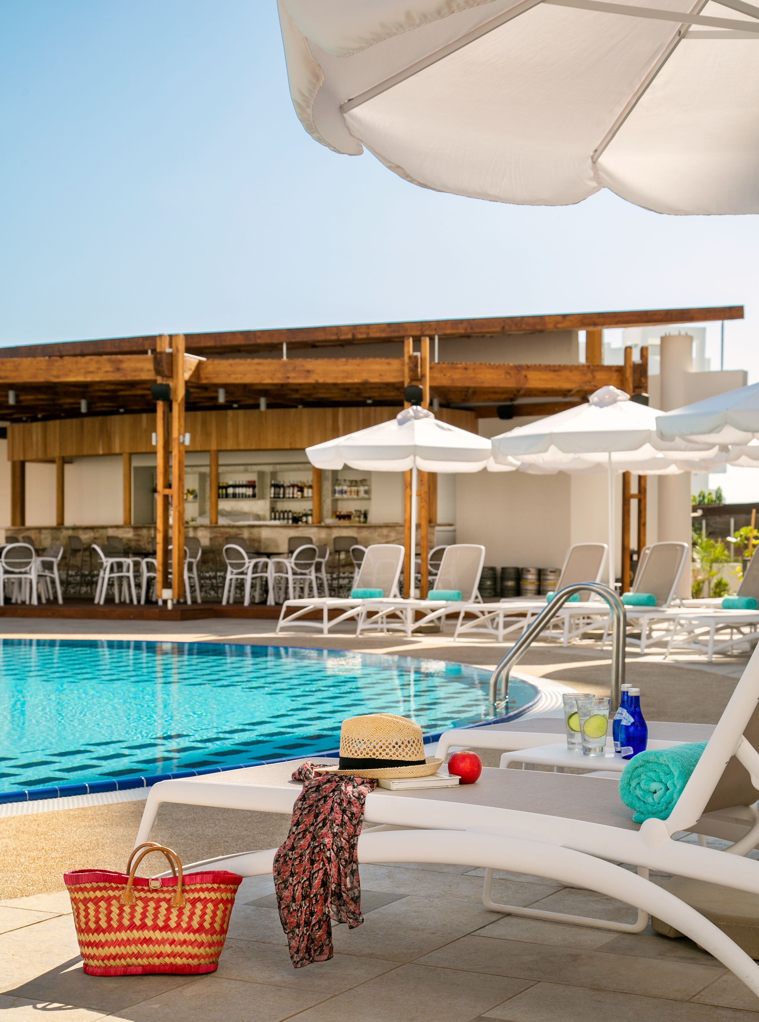 Zona junto a la piscina con sillones de descanso, sombrillas y una piscina.