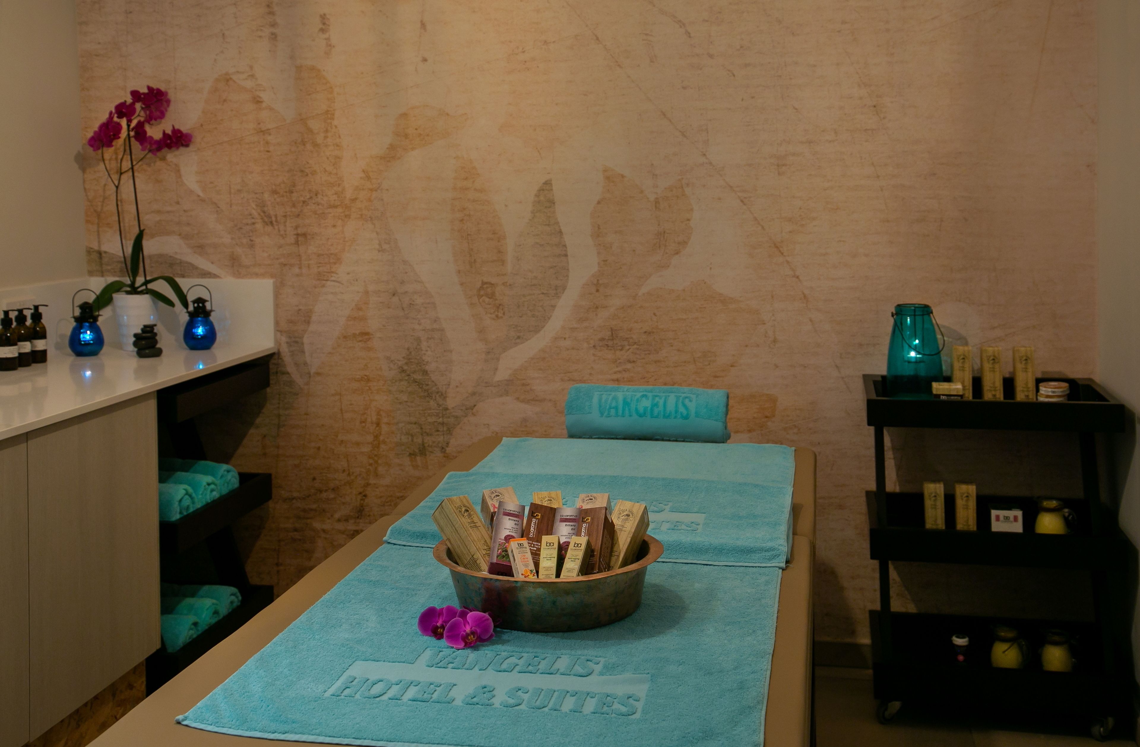 A room with a massage table, a bowl of toiletries, a vase with flowers, and a wall with a leaf pattern.
