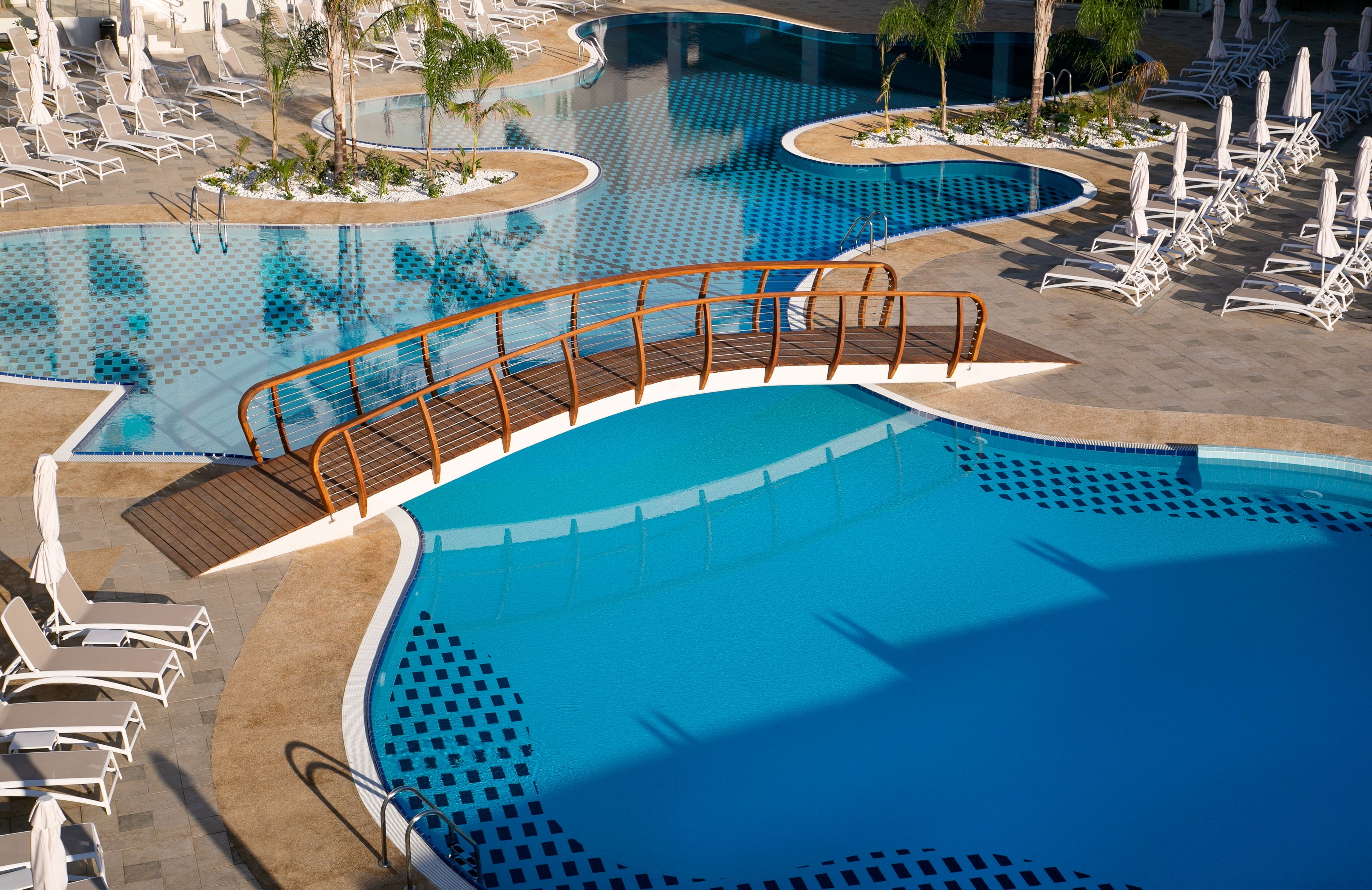 A large, clear blue pool with a wooden deck and lounge chairs.