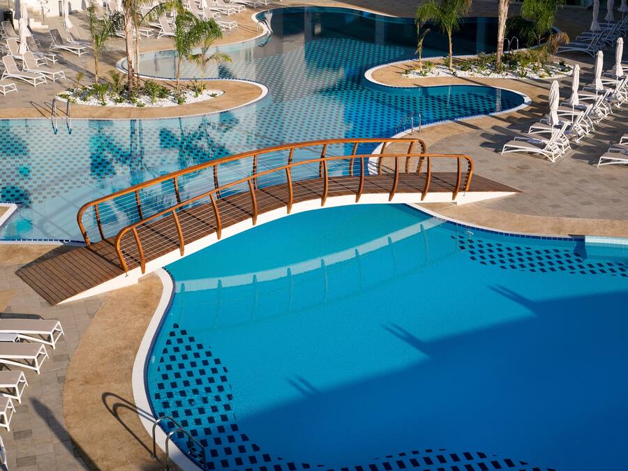 Ein großer, klarer blauer Pool mit einer Holzterrasse und Liegestühlen.